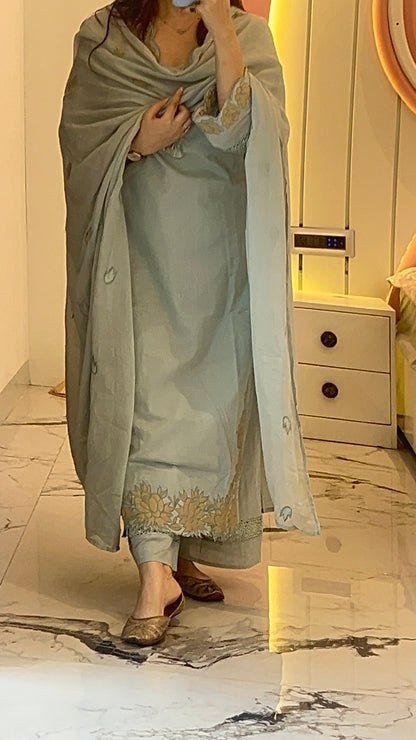 Person wearing a light gray traditional outfit with embroidery in a room.